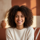 A smiling young adult in a close-up portrait, conveying trust and satisfaction. The background is softly blurred with warm, e